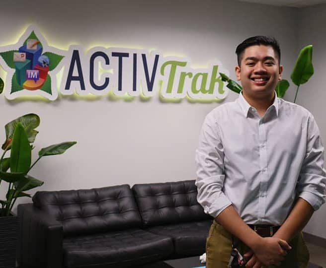 Tim Smaller standing in front of a black couch with plants on either side and the ActivTrak logo on the wall.