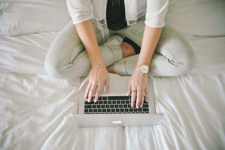 A woman sitting on a bed, working on a laptop using workforce analytics software.
