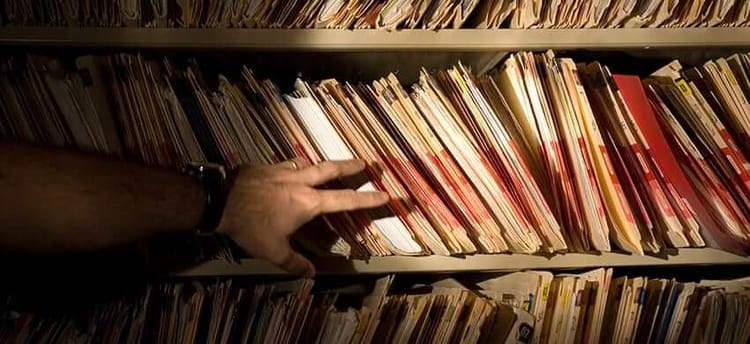 A man's hand reaching towards a bunch of file folders on a shelf.