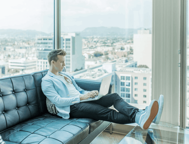 A man sitting on a couch, working on his laptop, with productivity monitoring, on a high level with a view overlooking a city.