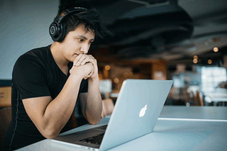 A man wearing headphones, staring intently at his laptop while experiencing employee burnout.
