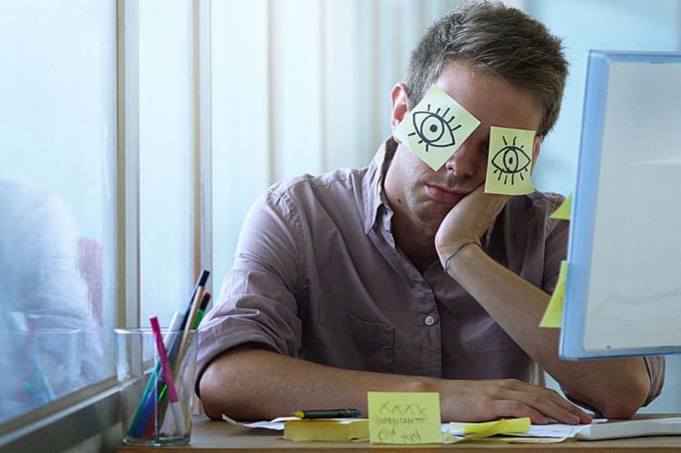 An employee sleeping at his desk with post-it notes over his eyes, making anyone wonder how to prevent quiet quitting.