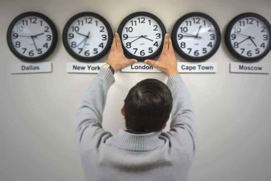 Five clocks in a row on a wall, each with a different city's name under it. A man adjusts the central one.