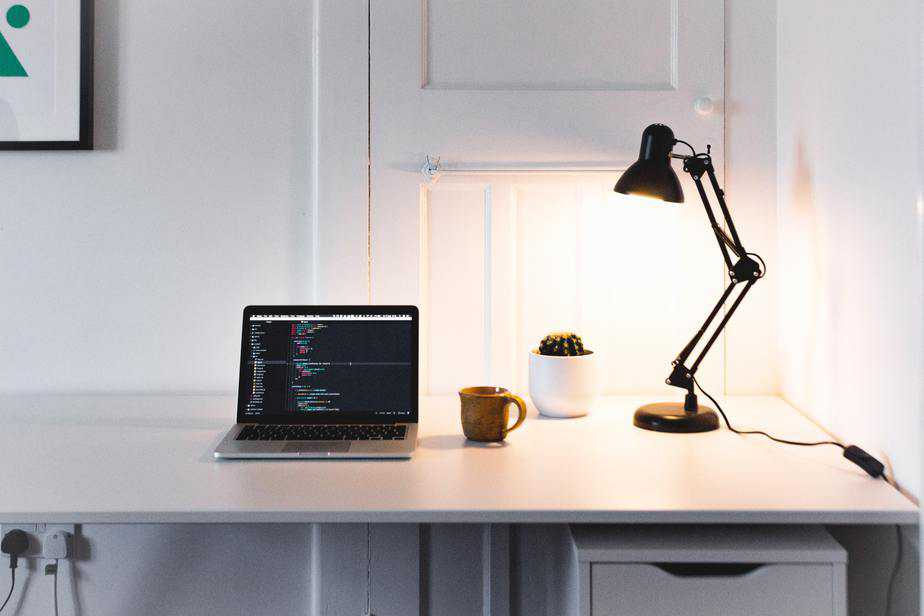 A desk in a home office with a laptop, lamp, plant and mug on it.