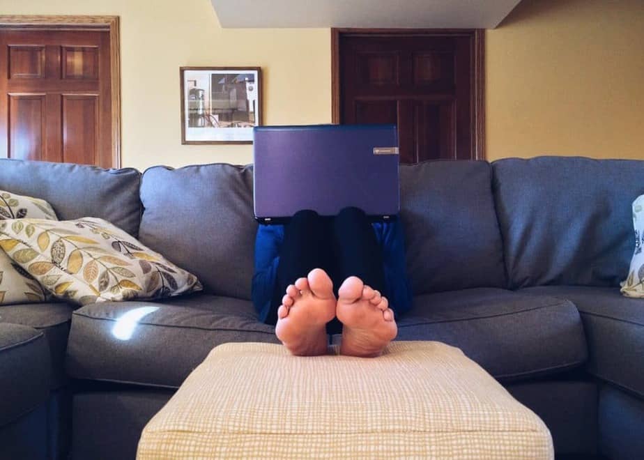 A person sitting on a couch with their feet up, with a laptop resting on their knees which is blocking their face.