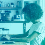 A woman working on her laptop, that uses employee monitoring software, on her kitchen table. Her phone is to her left.