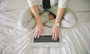 A woman sitting on a bed, working on a laptop using workforce analytics software.
