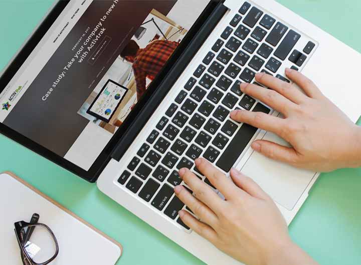 A pair of hands resting on the keyboard of a laptop that uses productivity monitoring software. A pair of glasses sit nearby.