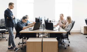 4 people working at a large table, each at their own computer, with employee monitoring software. One man is looking on.