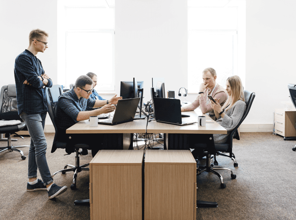 4 people working at a large table, each at their own computer, with employee monitoring software. One man is looking on.