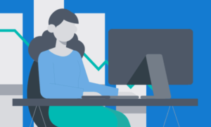 A woman sitting at a desk, working on a computer. There are graphs behind her.