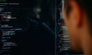 Seen from behind, a person looking at many lines of code on a large computer monitor, using productivity management software.