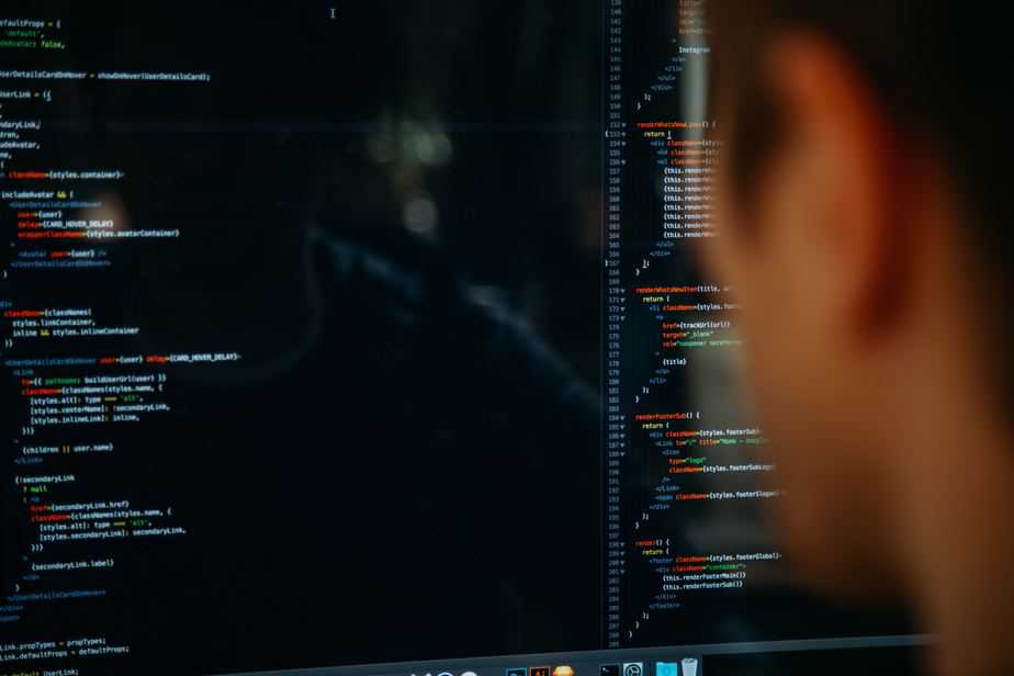 Seen from behind, a person looking at many lines of code on a large computer monitor, using productivity management software.