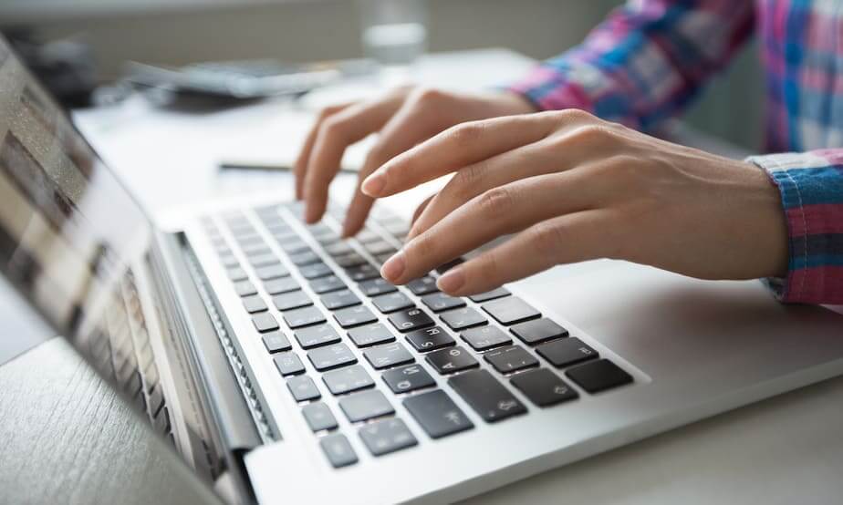 Hands typing on a laptop keyboard on a desk with remote workforce management software.