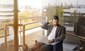 A man sitting on a balcony working on his laptop, which runs productivity monitoring software, on an upper story.