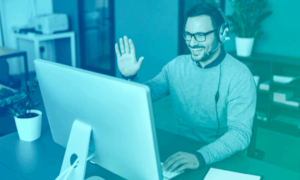 A man smiles and waves to his computer screen.