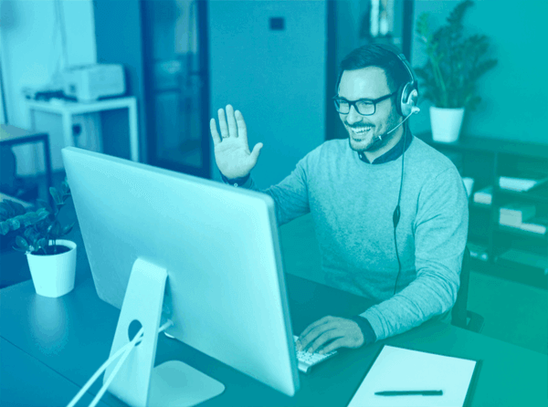 A man smiles and waves to his computer screen.