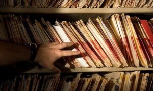A man's hand reaching towards a bunch of file folders on a shelf.