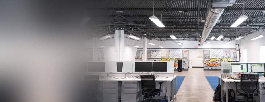 Several desks with two monitors on each, in an open warehouse used at office space.