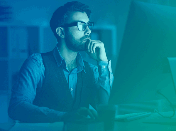 A man wearing a vest and glasses working at his computer, with workforce analytics software, in his home office.