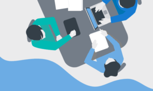 Seen from above, 3 people working at a table with a laptop, tablet, smart phone, folders and papers.