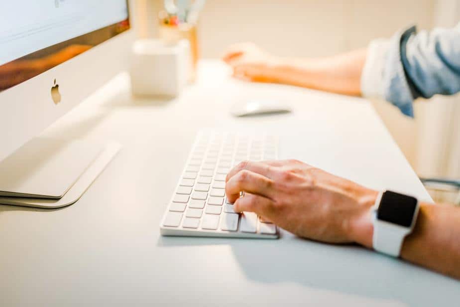 Hands typing on a keyboard of an Apple computer, which uses productivity measurement software and wearing an apple watch.