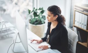 A woman in an office, typing on a keyboard at her desk, using productivity measurement software.