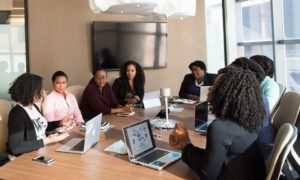 8 black women sitting around a conference table, each with a laptop in front of them that runs workforce analytics software.