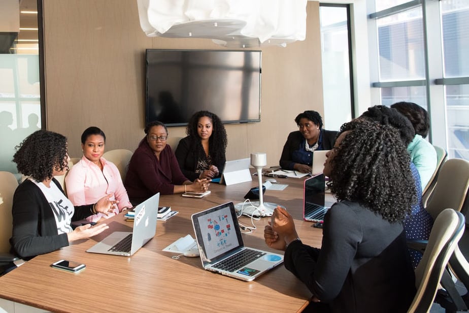 8 black women sitting around a conference table, each with a laptop in front of them that runs workforce analytics software.