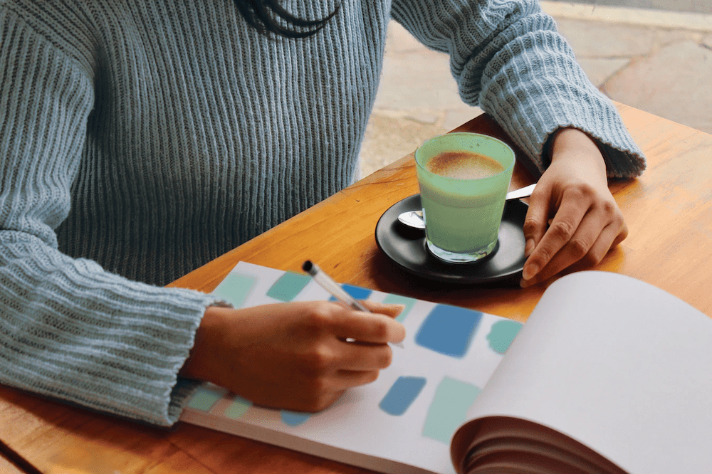 A woman writing in a notepad at a table in a café.