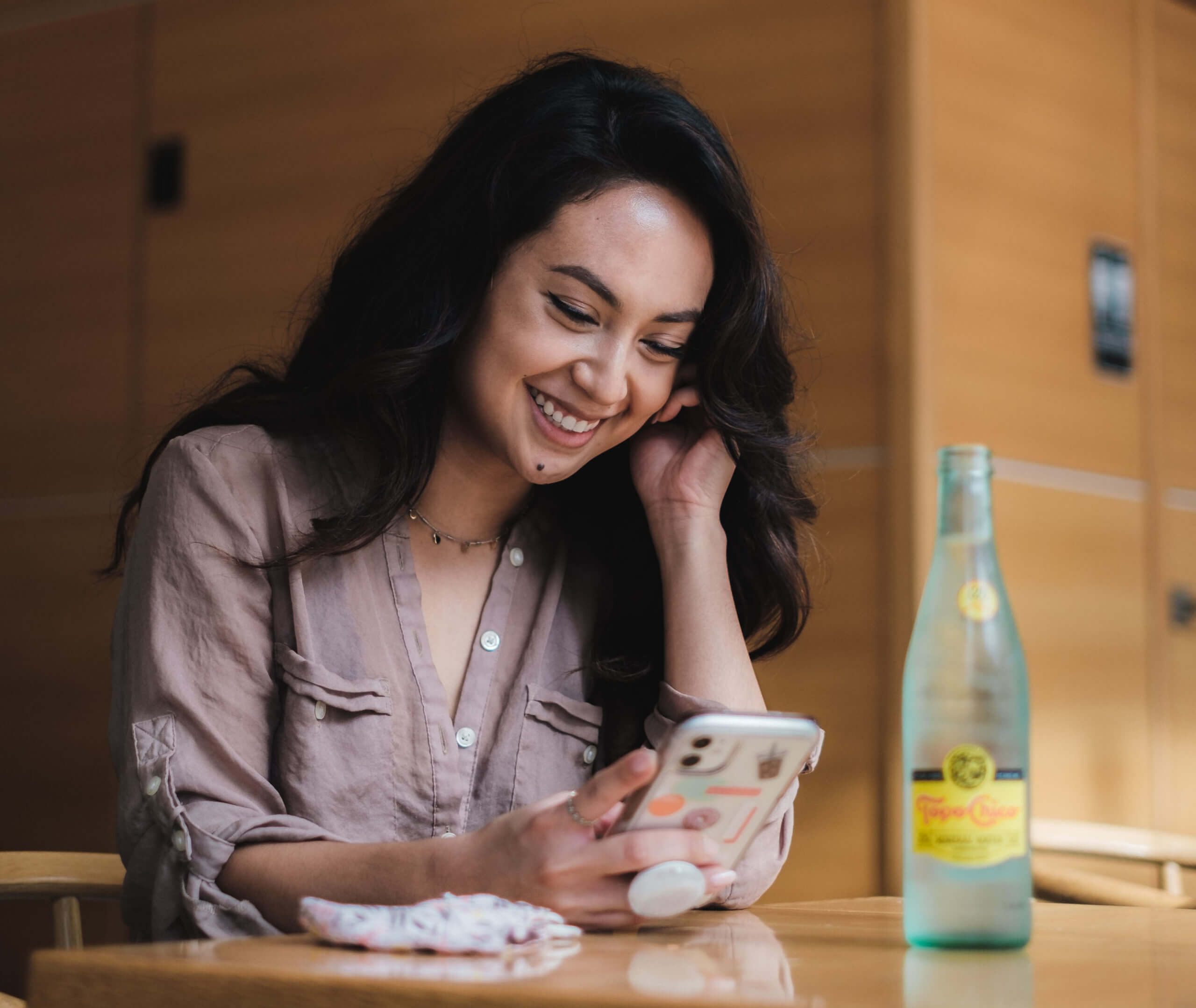 A woman in a restaurant laughing while looking at her phone.