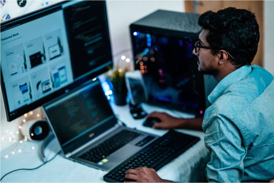 A man working at a desk with both a laptop and a computer on it, that run employee monitoring software.