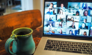 A laptop, with remote workforce management software, showing a Zoom meeting on a dining table with a coffee mug next to it.