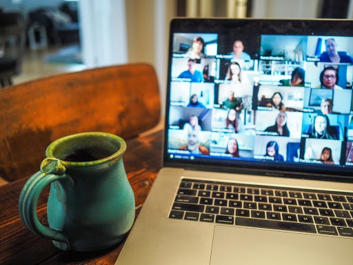 A laptop, with remote workforce management software, showing a Zoom meeting on a dining table with a coffee mug next to it.