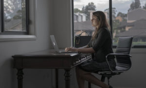 A woman sitting at a large desk in her home office typing on her laptop, which uses remote workforce management software.