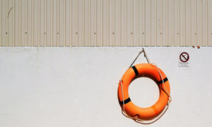 An orange life preserver hanging on a concrete wall.