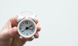 A hand holding a small, white, analog alarm clock.