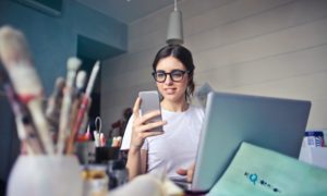 A woman sitting at her desk with her laptop looking at her phone