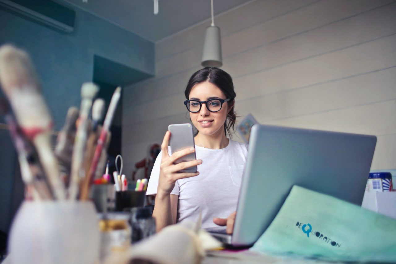 A woman sitting at her desk with her laptop looking at her phone