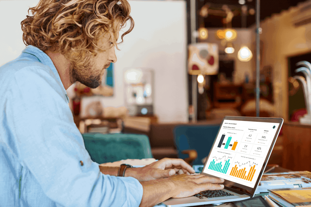 A man working at a table in a café on his laptop which shows ActivTrak productivity measurement reports.