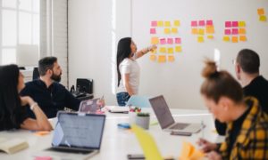 A woman working on a whiteboard in an office full of people