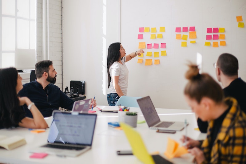 A woman working on a whiteboard in an office full of people