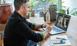 A man sitting at a table in his home, having a Zoom meeting with a woman, and using productivity management software.
