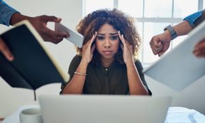 A woman looking distressed with her hands at her temples while people around her put a book and different devices in her face.