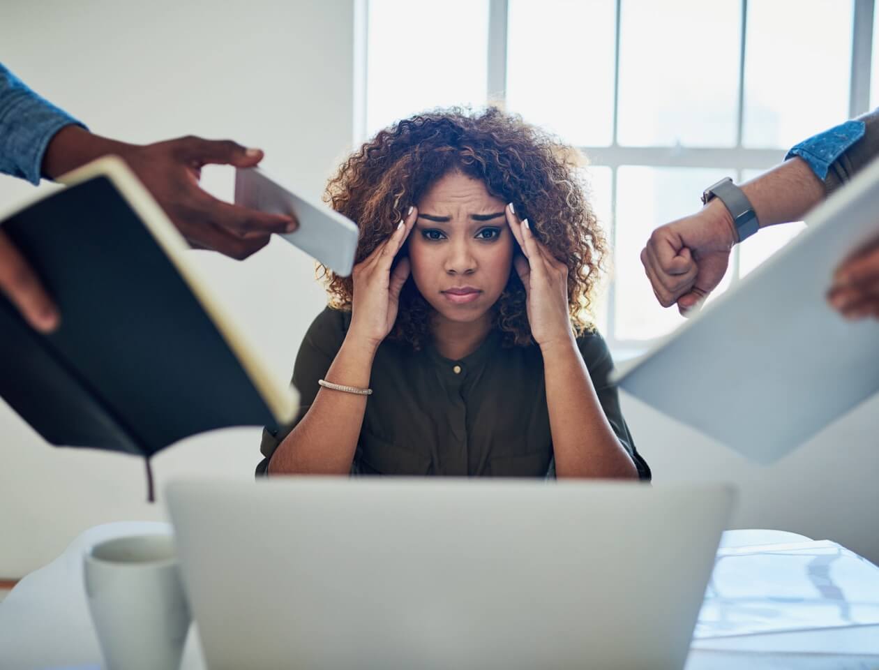 A woman looking distressed with her hands at her temples while people around her put a book and different devices in her face.