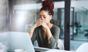 A woman sitting at a desk, looking worried, about employee monitoring software, with her hand on her forehead.