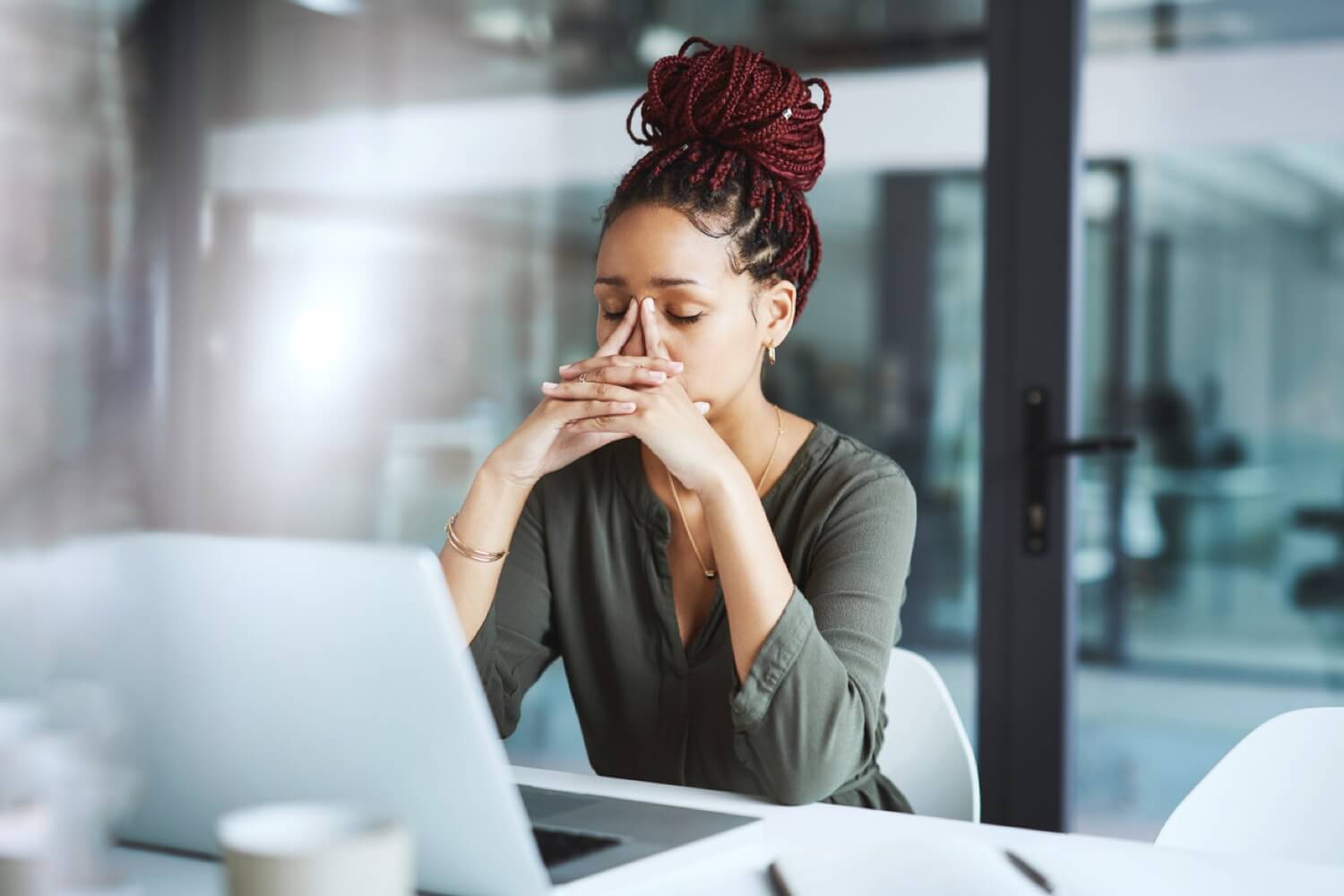 A woman sitting at a desk, looking worried, about employee monitoring software, with her hand on her forehead.