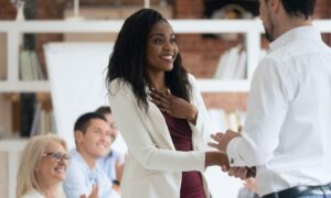 Manager showing appreciation to an employee in front of a group in an office.