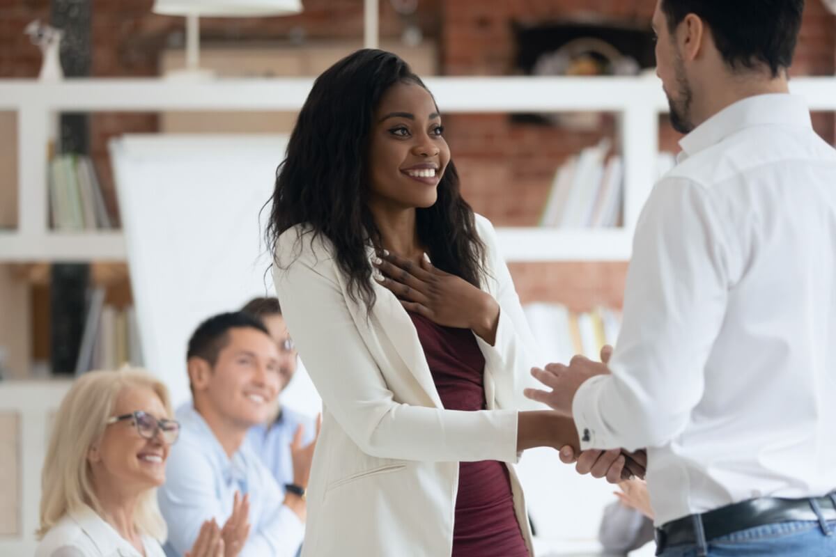 Manager showing appreciation to an employee in front of a group in an office.