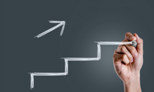 An employee drawing on a whiteboard - stairs and an arrow pointing up and to the right to signal stepping up work productivity.